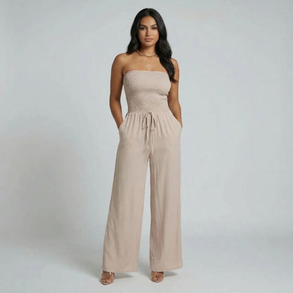 Beige strapless smocked jumpsuit with waist tie and side pockets — front view.
