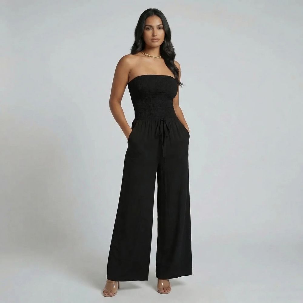Black smocked strapless jumpsuit with flowing wide-leg design — front view styled with heels.