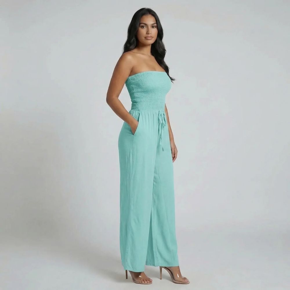 Blue smocked strapless jumpsuit with adjustable waist tie — angled view.