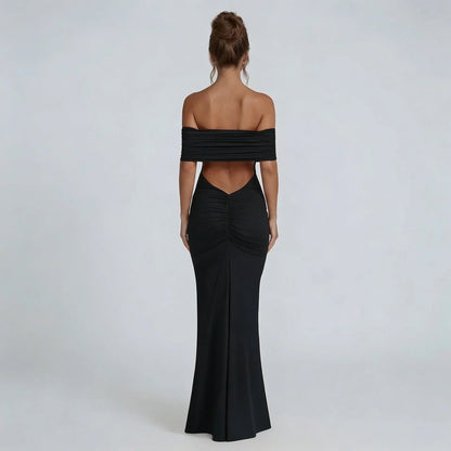 Black off-shoulder ruched maxi dress with ruched back seam — rear view showcasing bold open back and tapered silhouette.