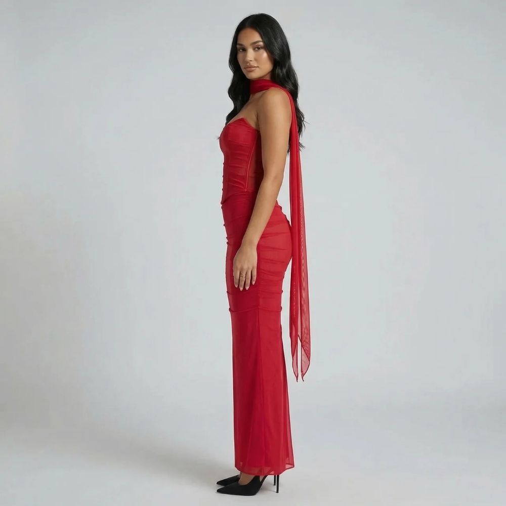 Red ruched maxi dress with fluted hem and corset-style bodice — side view highlighting structure and scarf detail.