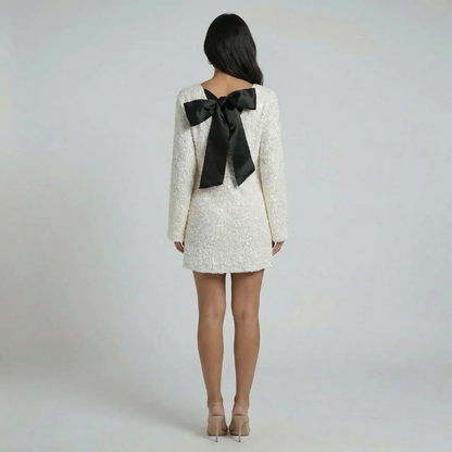 White sequin shift mini dress with oversized black bow detail — back view showing dramatic bow accent.